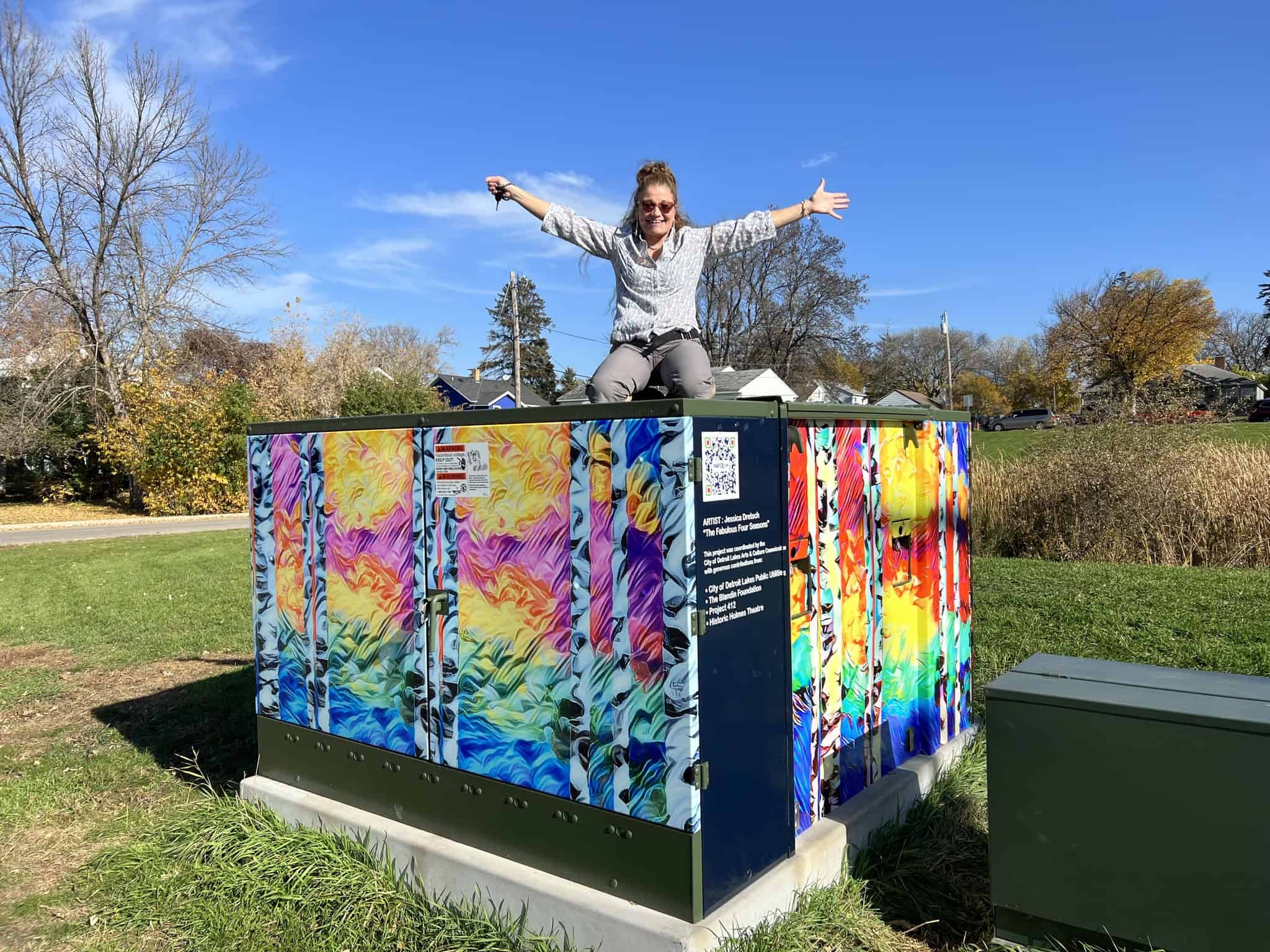 "The Fabulous Four Seasons" power box art wrap • Jessica Dretsch on top of the power box • behind Sanford clinic • Artist: Jessica Dretsch • Power box created in coordination with Arts & Culture Commission and the City of Detroit Lakes Public Utilities