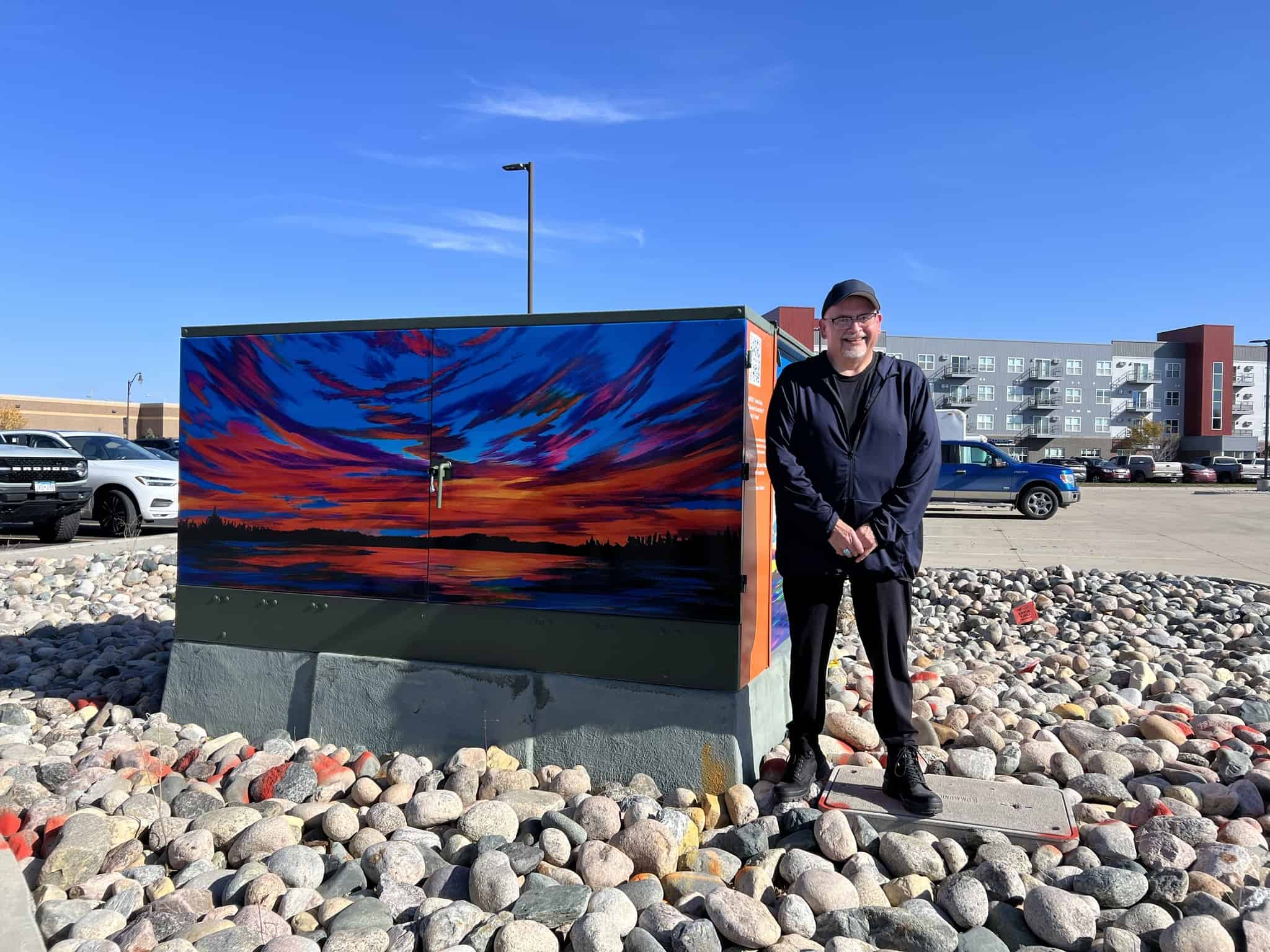 "Summer Sunset No. 1" & "Best of Times" power box art wrap • Kent Estey next to the power box art • Artist: Kent Estey • Power box created in coordination with Arts & Culture Commission and the City of Detroit Lakes Public Utilities