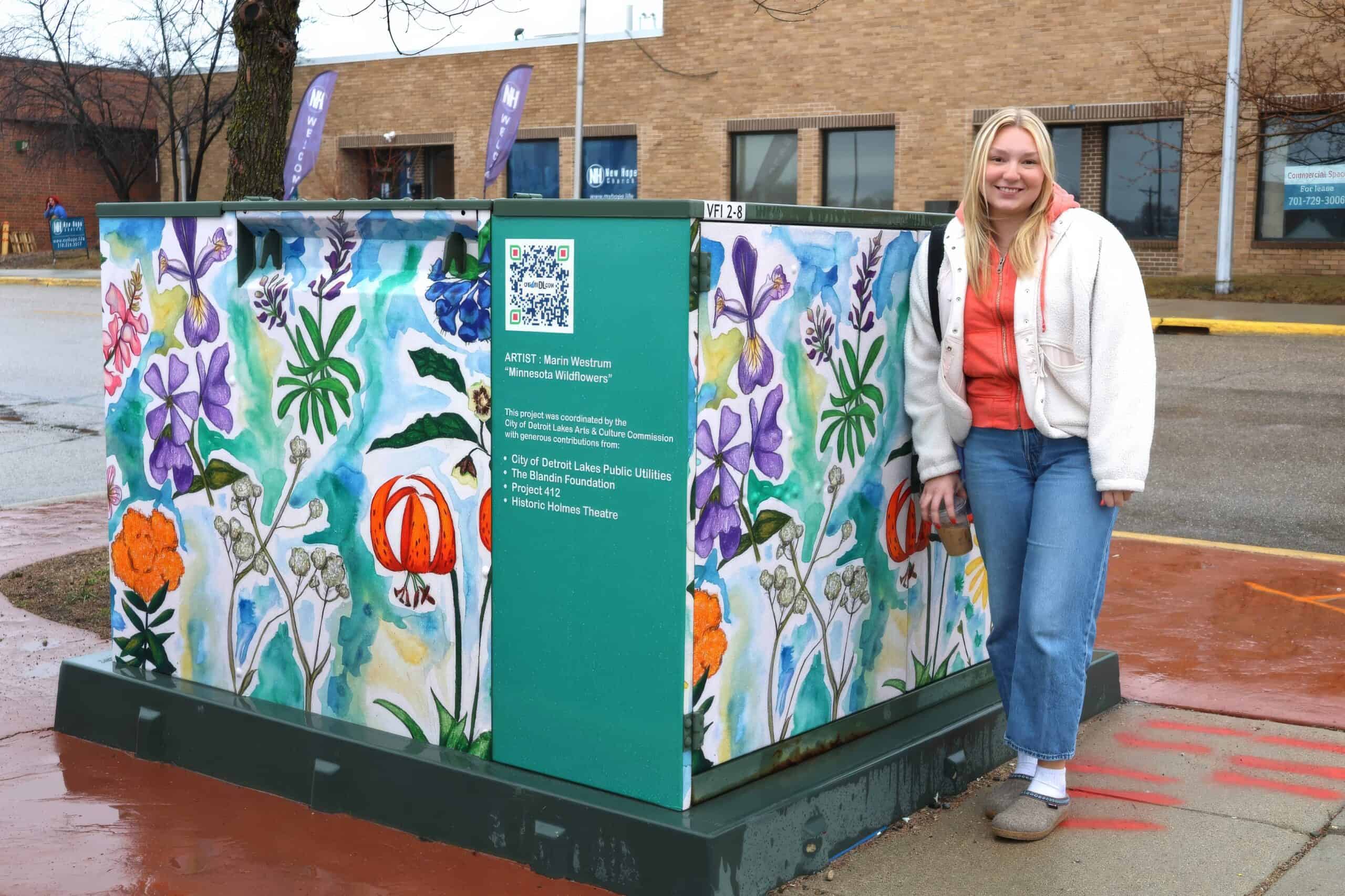 "Minnesota Wildflowers" power box art wrap • Artist: Marin Westrum, standing next to the art • Power box created in coordination with Arts & Culture Commission and the City of Detroit Lakes Public Utilities